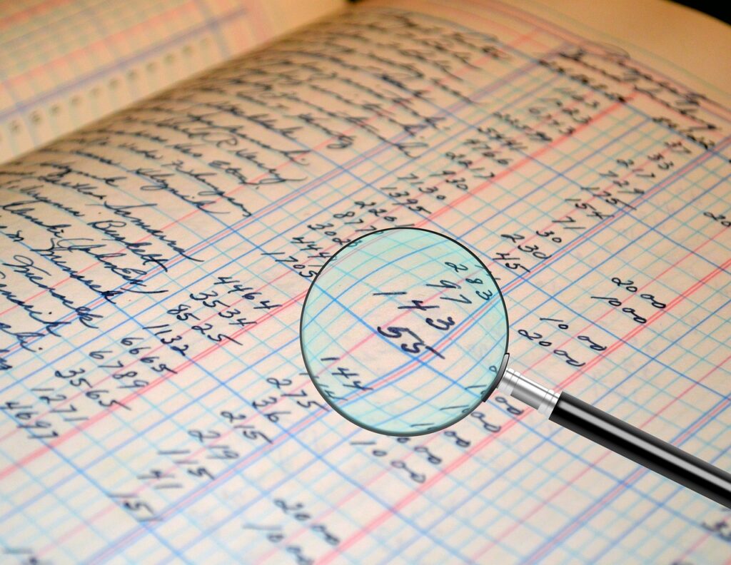 Magnifying glass over a paper ledger, the way an auditor walks a small contractor's books during a preaward survey