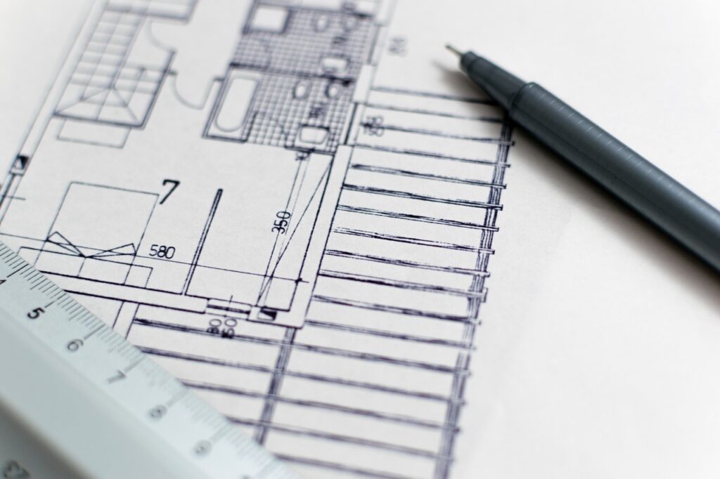 Construction floor plans and a pen, representing the solicitation attachments a contractor reads alongside a Davis-Bacon wage determination
