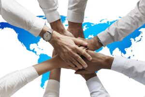 Hands of business partners stacked together over a world map, like firms teaming up to win a federal contract