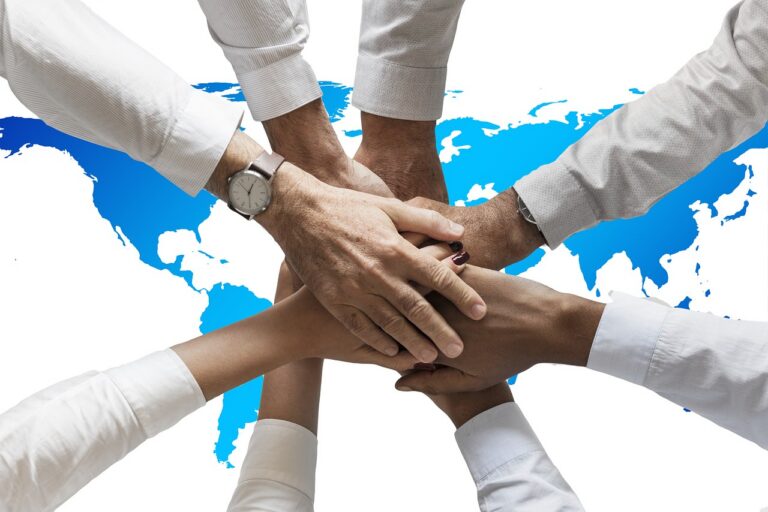 Hands of business partners stacked together over a world map, like firms teaming up to win a federal contract