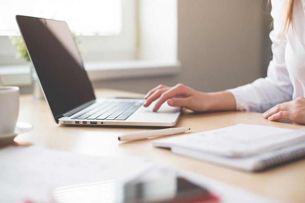 Business owner filling out a WOSB certification application on a laptop, with supporting records on the desk