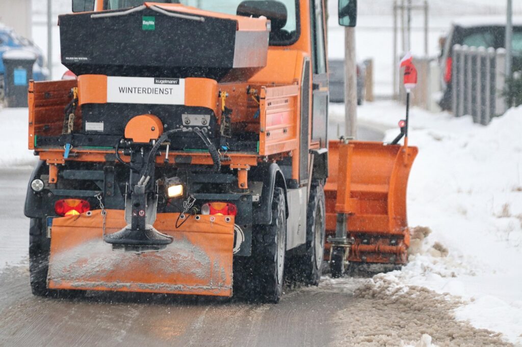Snow plow truck with a salt spreader clearing a street