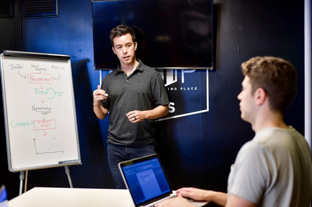 Experienced contractor coaching a newer small business owner at a whiteboard, as a mentor does for a protégé